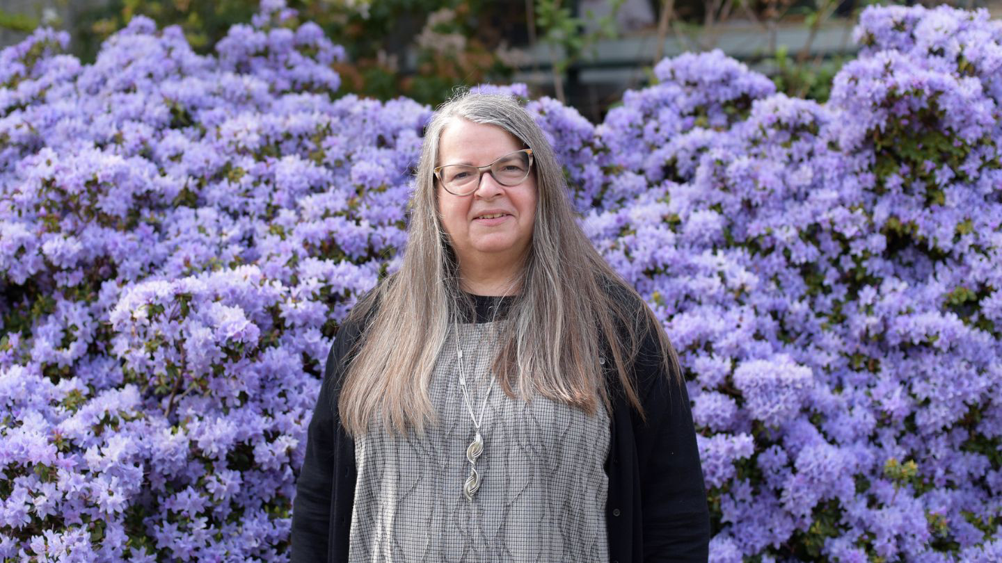 Monica Prendergast is pictured outdoors on campus in front of purple blooming flowers. 