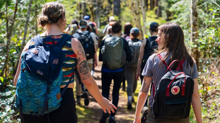 Two students leading an outdoor camp group during coop. They are pictured from behind, walking through the forest at the back of their group.