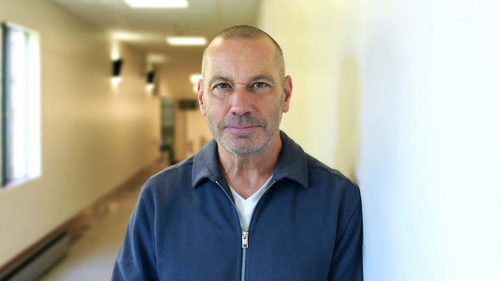 A portrait of Dr. Todd Milford. He is pictured in a hallway in MacLaurin Building, wearing a navy blue knitted sweater and looking into the camera lens.