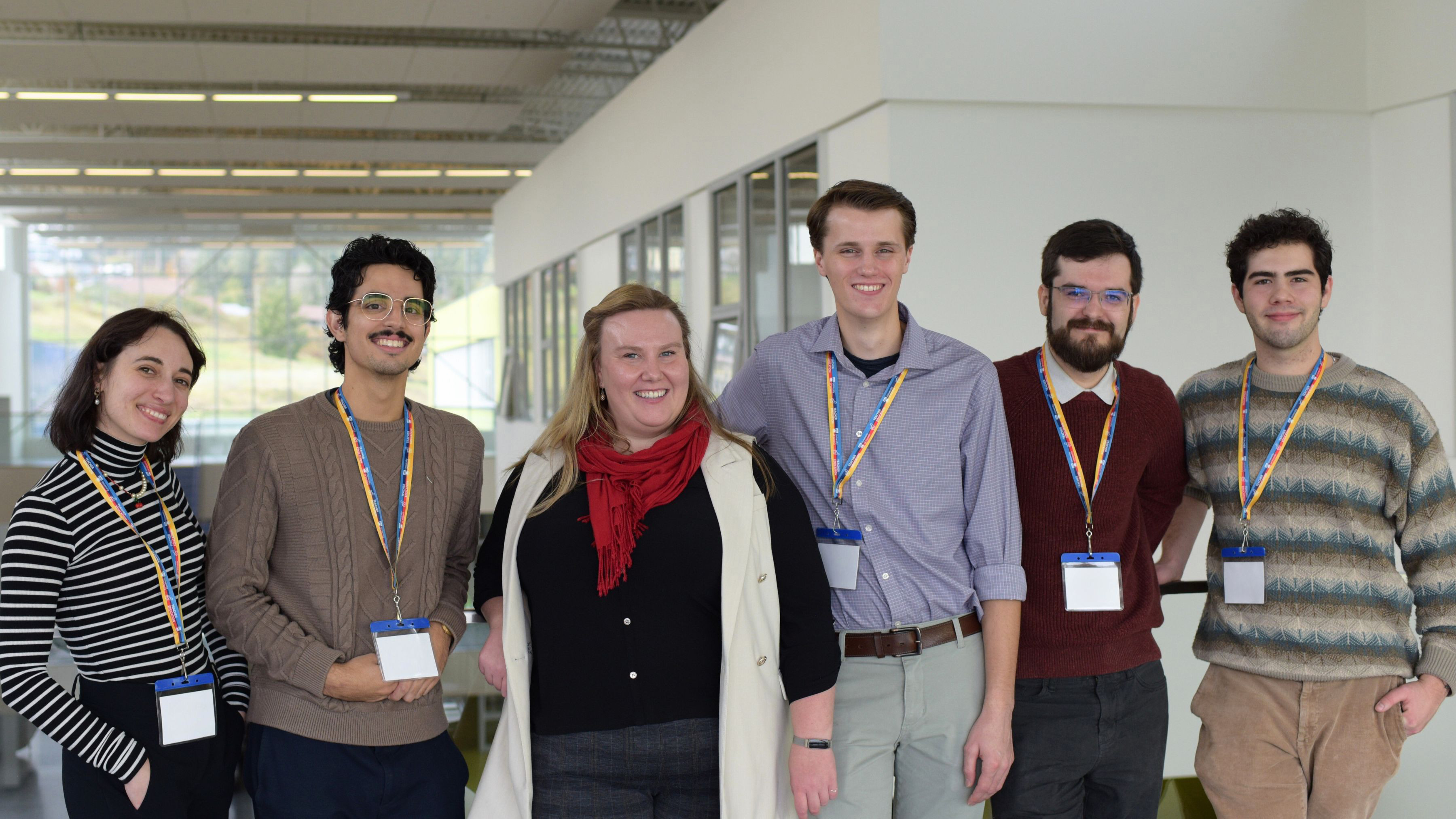 A group of six students are pictured together in a secondary school environment. Most of them are wearing UVic lanyards, suggesting they are visiting the school from UVic. The students are smiling and facing toward the camera.