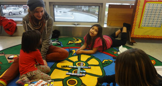 Tutor works with a student on a patterning puzzle on the carpet at Kwum Kwum Lelum