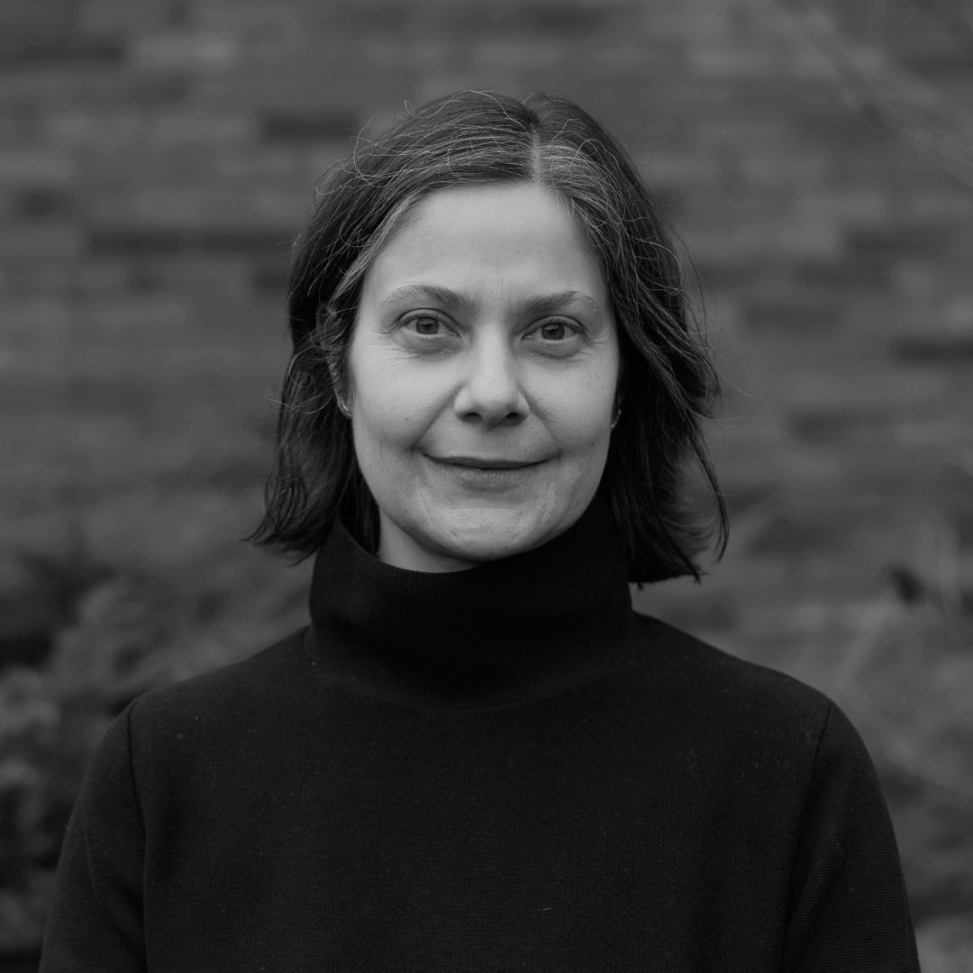 A black and white head and shoulders portrait of Barbara Jenni, pictured outdoors on campus in front of the MacLaurin Building. She is looking into the camera lens with a neutral expression, wearing a black turtleneck.