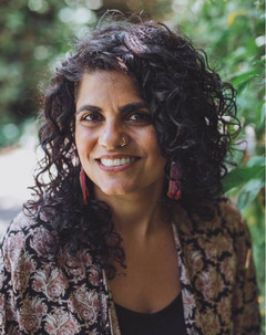 A head-and-shoulders portrait of Mandeep Kaur Mucina on campus. They are pictured outdoors, wearing a colourful top and long red beaded earrings.