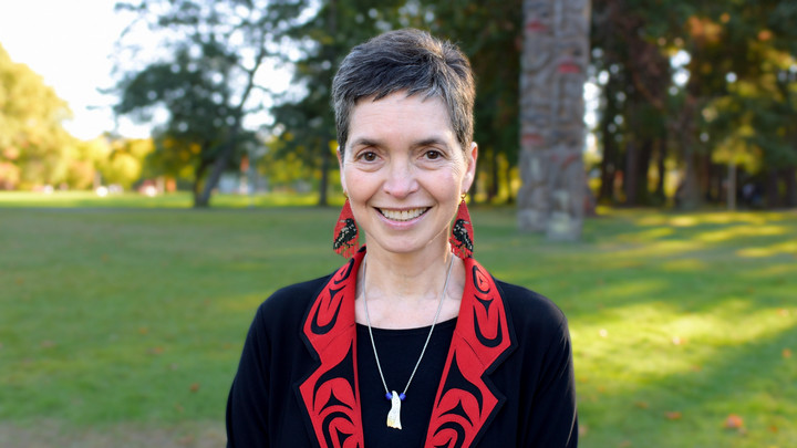 A portrait of Edosdi outdoors on campus on a sunny day. She is wearing red beaded earrings with black crows on them