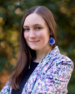 A portrait of wiigwaas pictured outdoors, she is wearing a purple patterned blazer and purple beaded earrings.