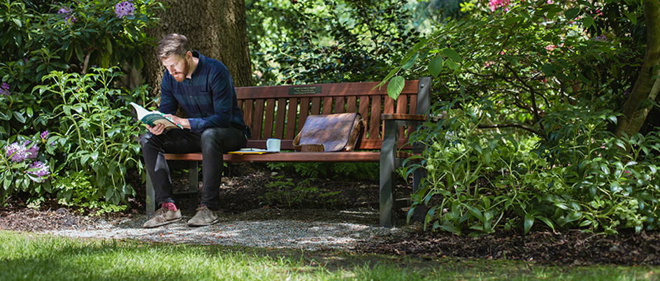 Student sitting on a bench on the UVic campus surrounded by lush plants