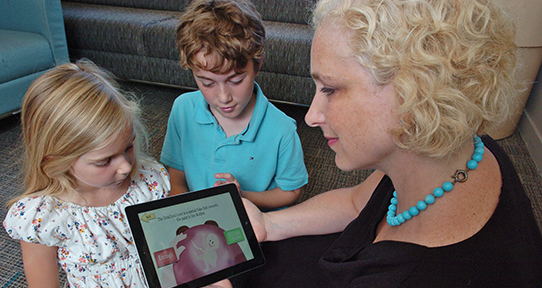 Jillian Roberts showing two kids her app on a tablet