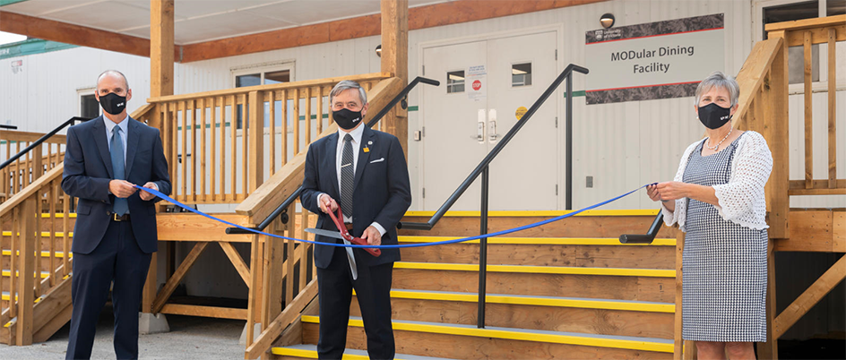 Saanich mayor Fred Haynes holds large scissors, preparing to cut a blue ribbon in front of the new modular dining facility.