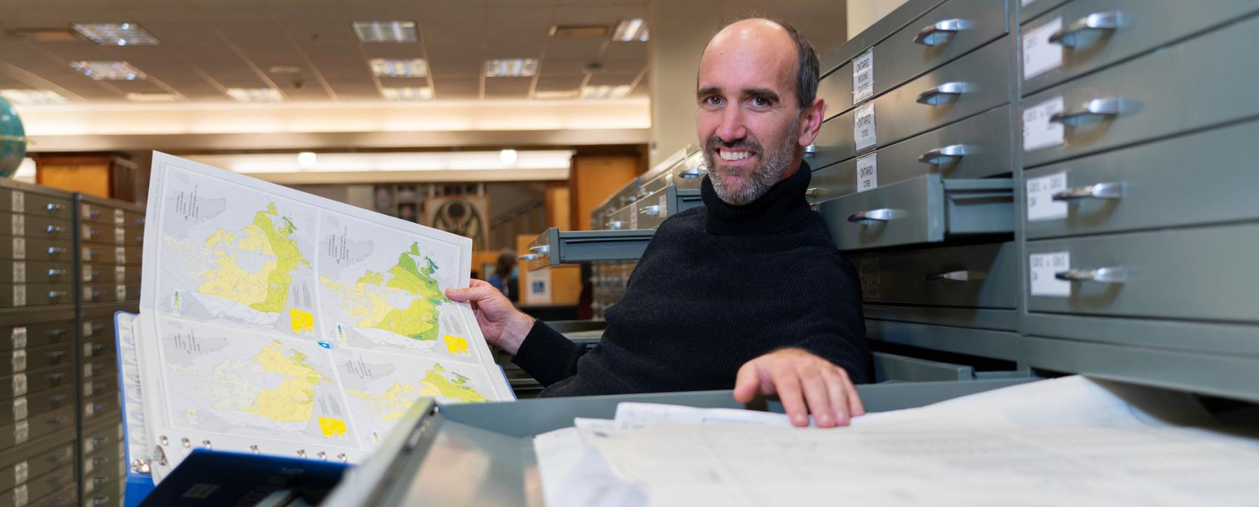 Professor Tom Gleason holds a map while seated at UVic Library