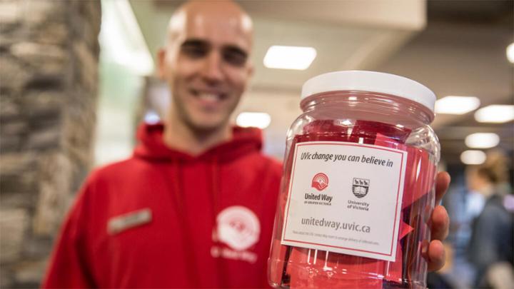 A UVic employee wearing a red United Way hoodie holds a jar containing raffle tickets.