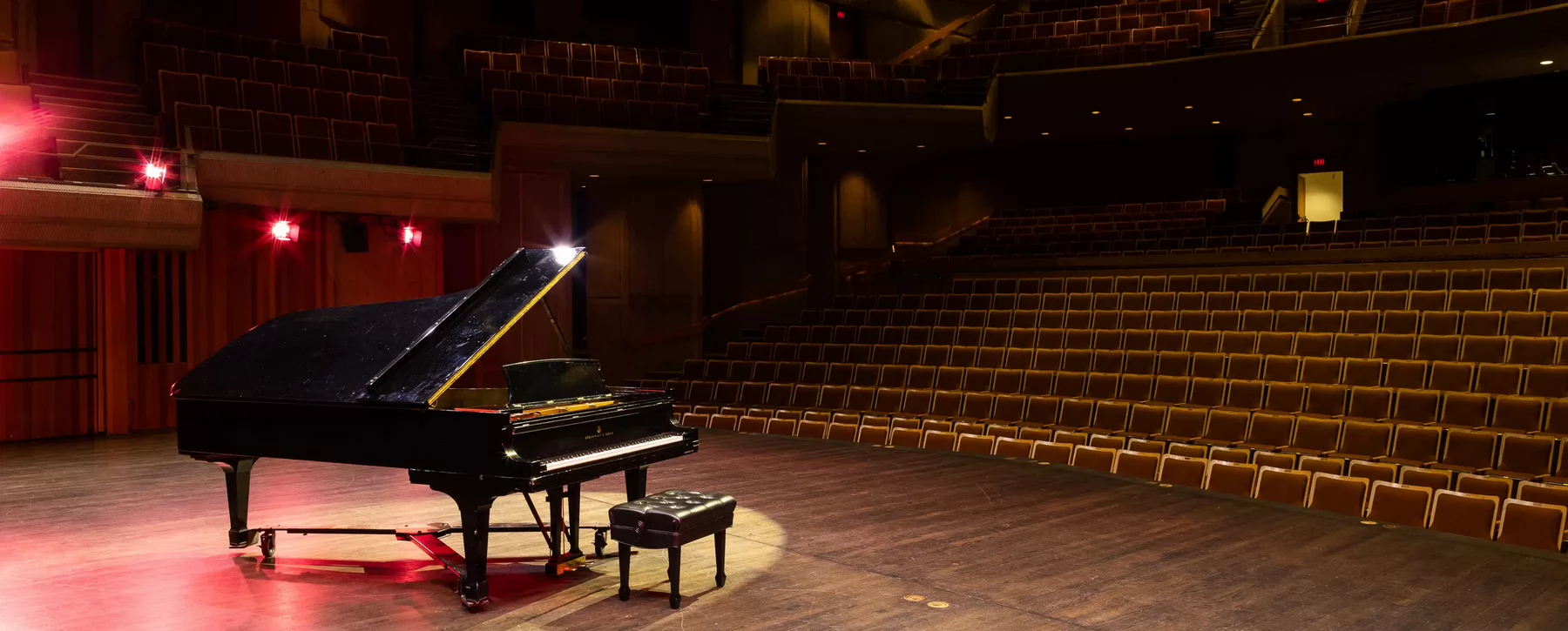 Piano facing rows of seat with red lighting.