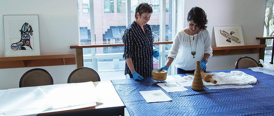 Two women handling artifacts on a table