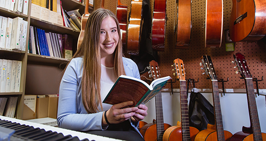 Jilaine Orton reading a music book by a piano and guitars