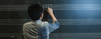 Student writing music notes on a chalkboard