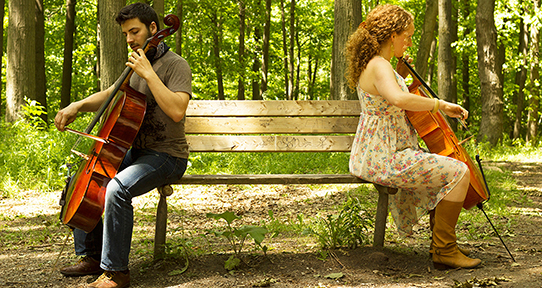 Eli Bender and Rachel Capon playing cellos on a park bench