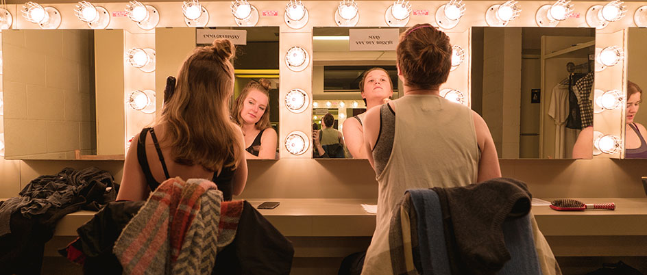 Two women looking into mirrors preparing for a performance