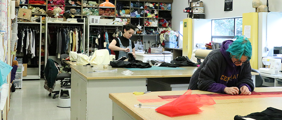 Two students sew in a costume shop. 