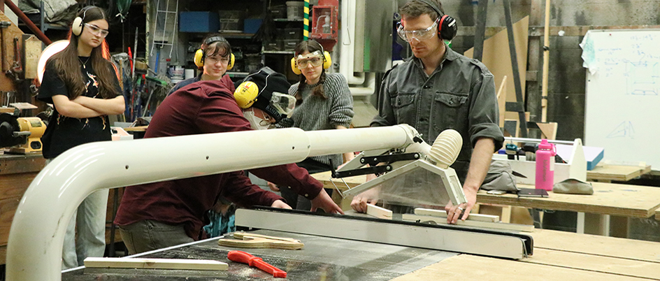 A group of students using a table saw under the supervision of a teacher.