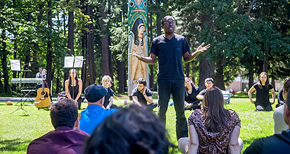 Taiwo Afolabi speaking to a group of students circled around him on the UVic campus outdoors