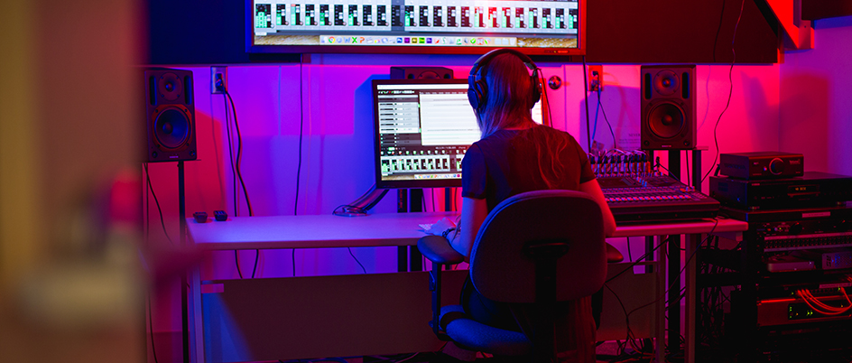 Female student in a music lab looking at a computer plugged into a sound board