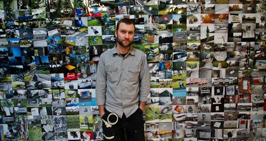 Artist and alumnus Mike McLean standing in front of a wall filled with photographs