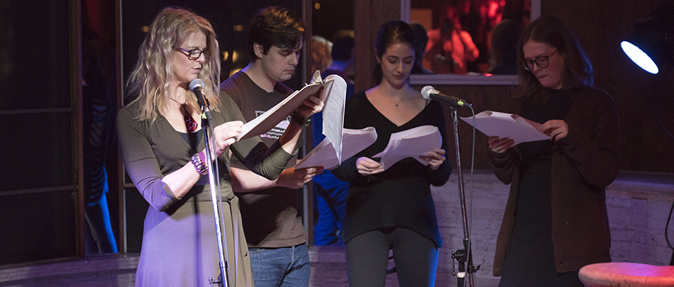 Students reading into microphones on a small stage