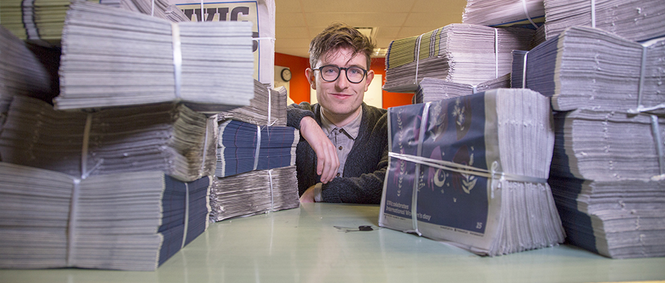 Student sitting with stacks of newspapers