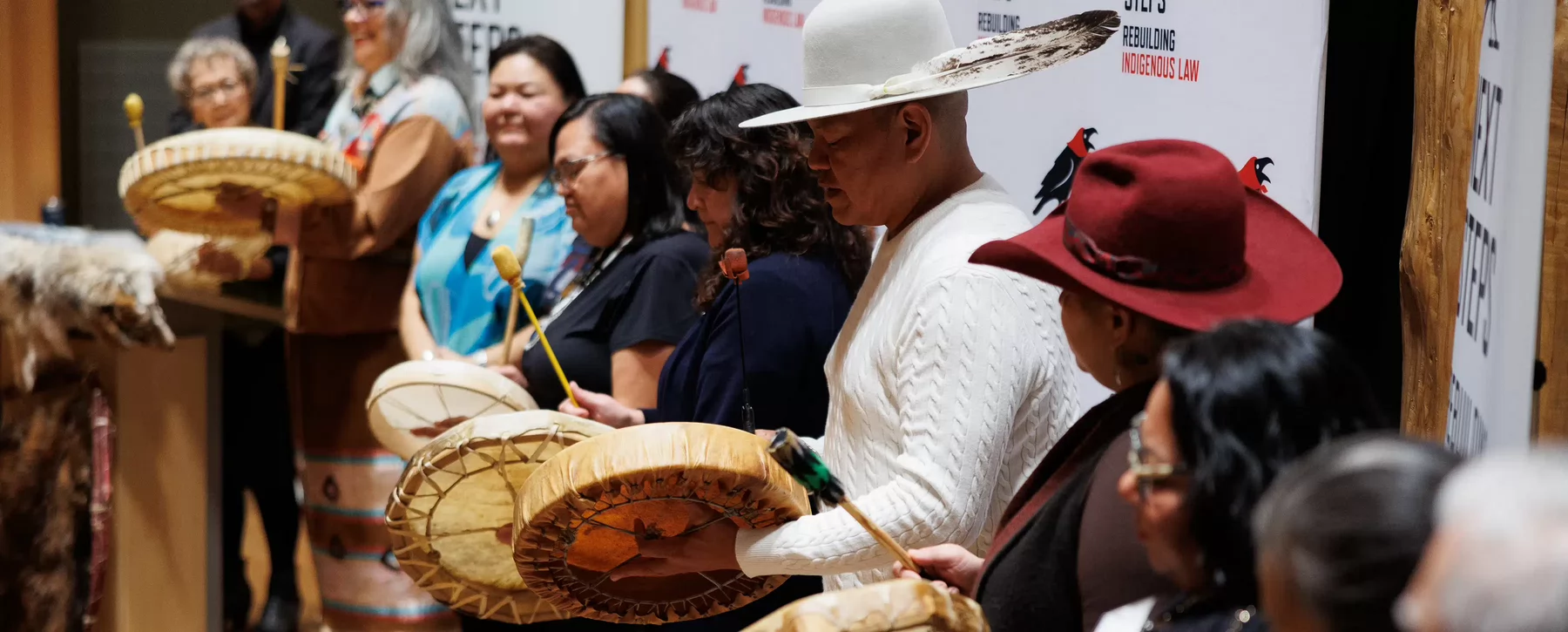 Eight people in a line, some holding traditional drums, singing