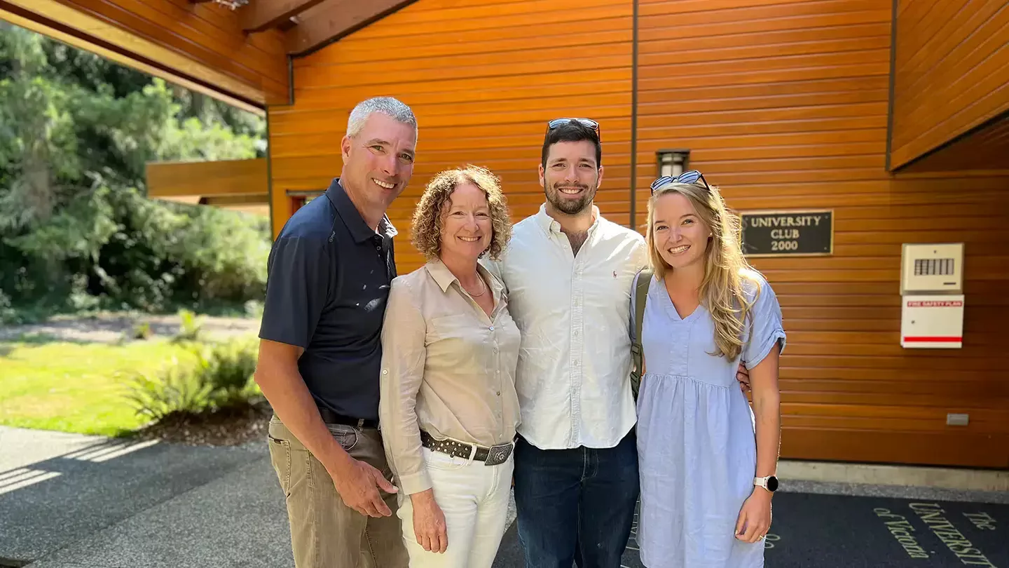 An adult family of four smiling while standing outside the University Club.