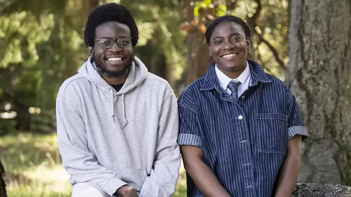 Two students sitting side by side outside smiling.