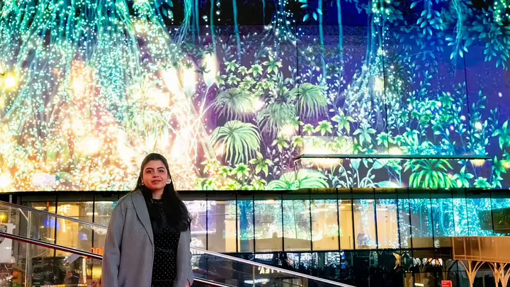 A woman standing in front of a digital image of a tree on a digital billboard in New York City's Times Square.