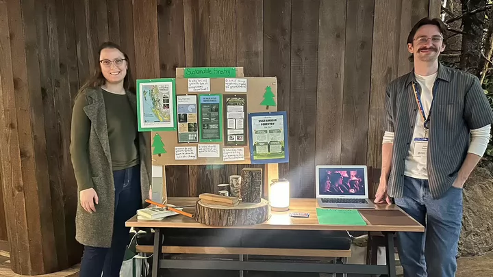 Two undergraduate students stand at a learning station about sustainable forestry at the Royal BC Museum.