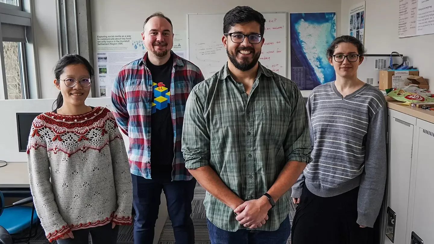 Four people standing side by side in an office space with white boards and a map in the background. 