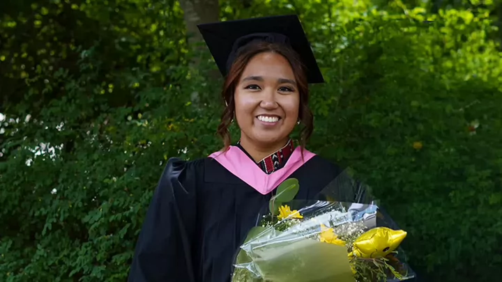 University of Victoria graduate in convocation gown holding a bouquet outdoors.