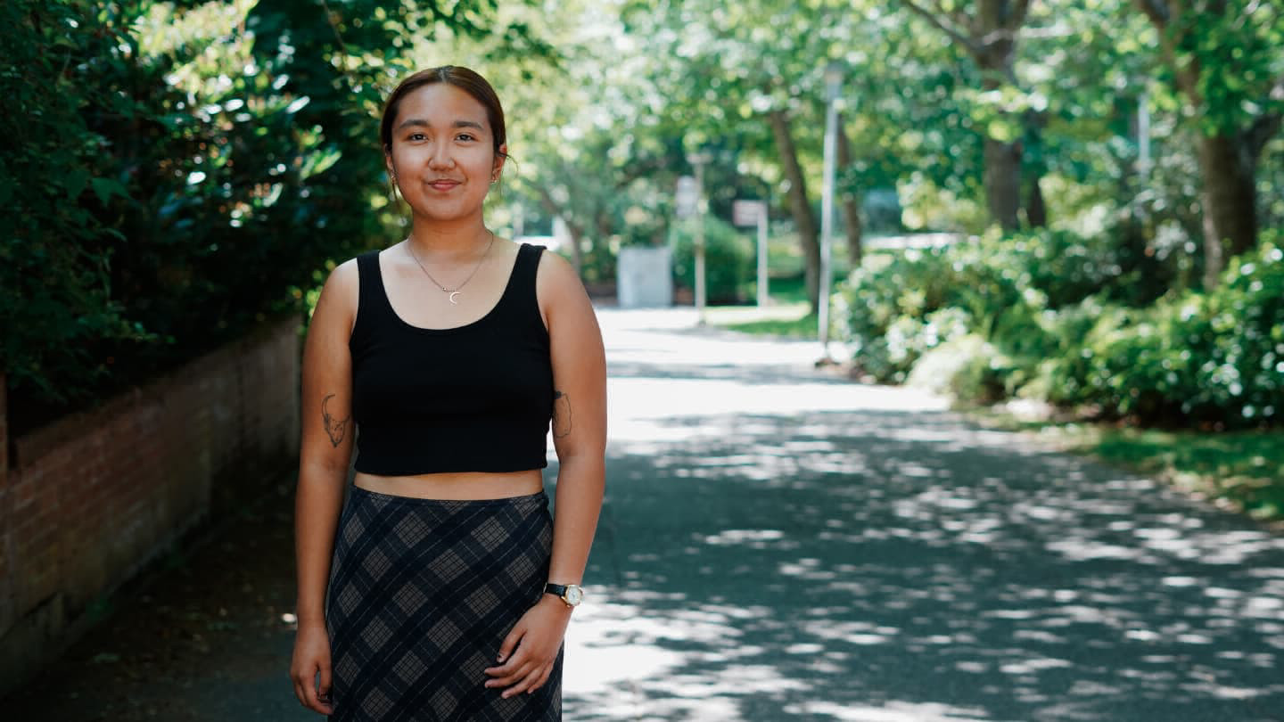 Person standing on a shaded path surrounded by trees and greenery.