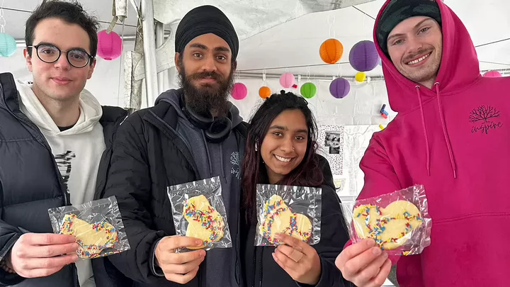 Four students at an event hold up cookies toward the camera