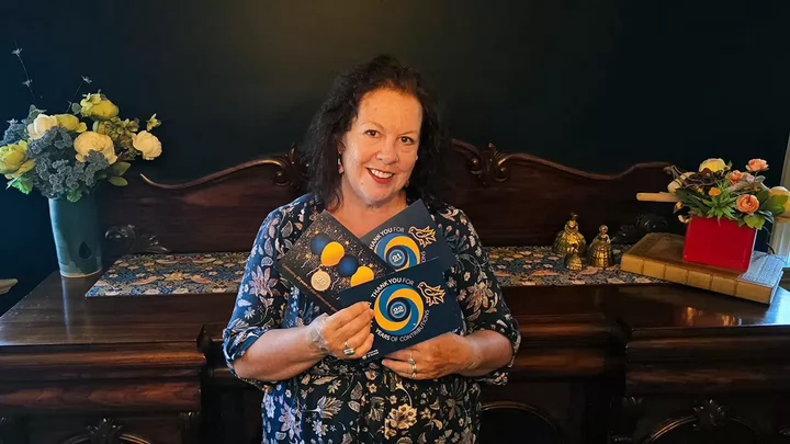 A woman wearing a flowery shirt and smiling while holding up several postcards that say Thank You For 22 Years of Contributions. 