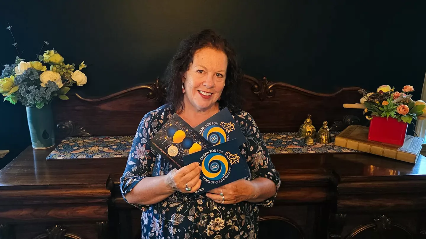 A woman wearing a flowery shirt and smiling while holding up several postcards that say Thank You For 22 Years of Contributions. 