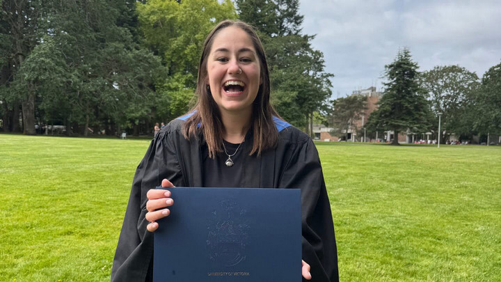 Jayda smiling, holding her graduation certificate in her graduation gown.