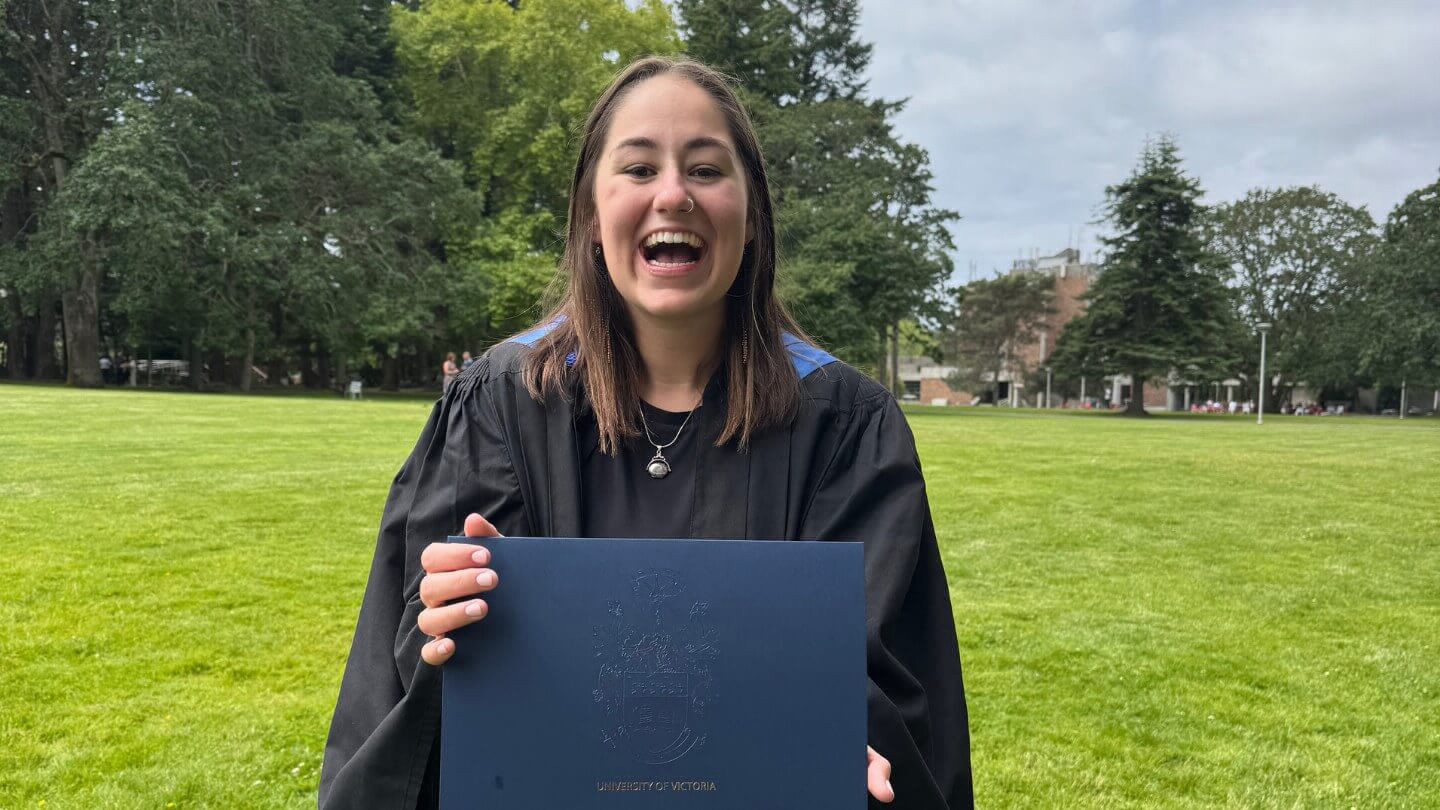 Jayda smiling, holding her graduation certificate in her graduation gown.
