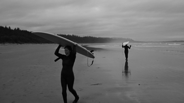 Jayda walking on the beach holding a surf board above her head.
