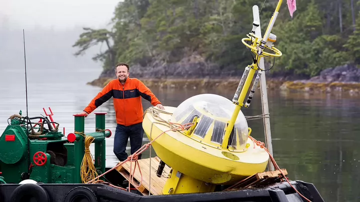 Man standing on a boat containing a buoy equipped with sensors.