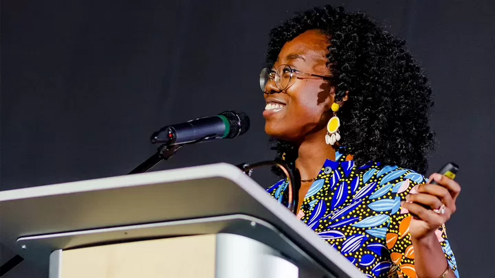 A woman at podium smiling while giving a presentation.