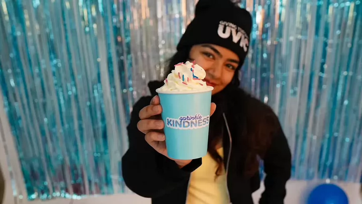 A student wearing a toque that says UVic Giving Tuesday holding a sprinkled covered coffee drink that says Sprinkle Kindness.