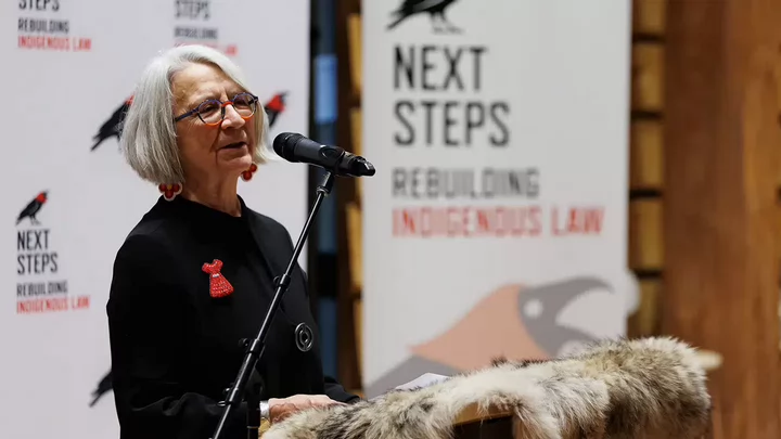 Val speaking at a lectern in front of a banner that reads Next Steps