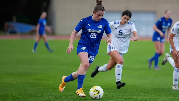 A woman wearing the number 29 on her UVic Vikes soccer uniform dribbles a soccer ball down field past her opponent during a game. 