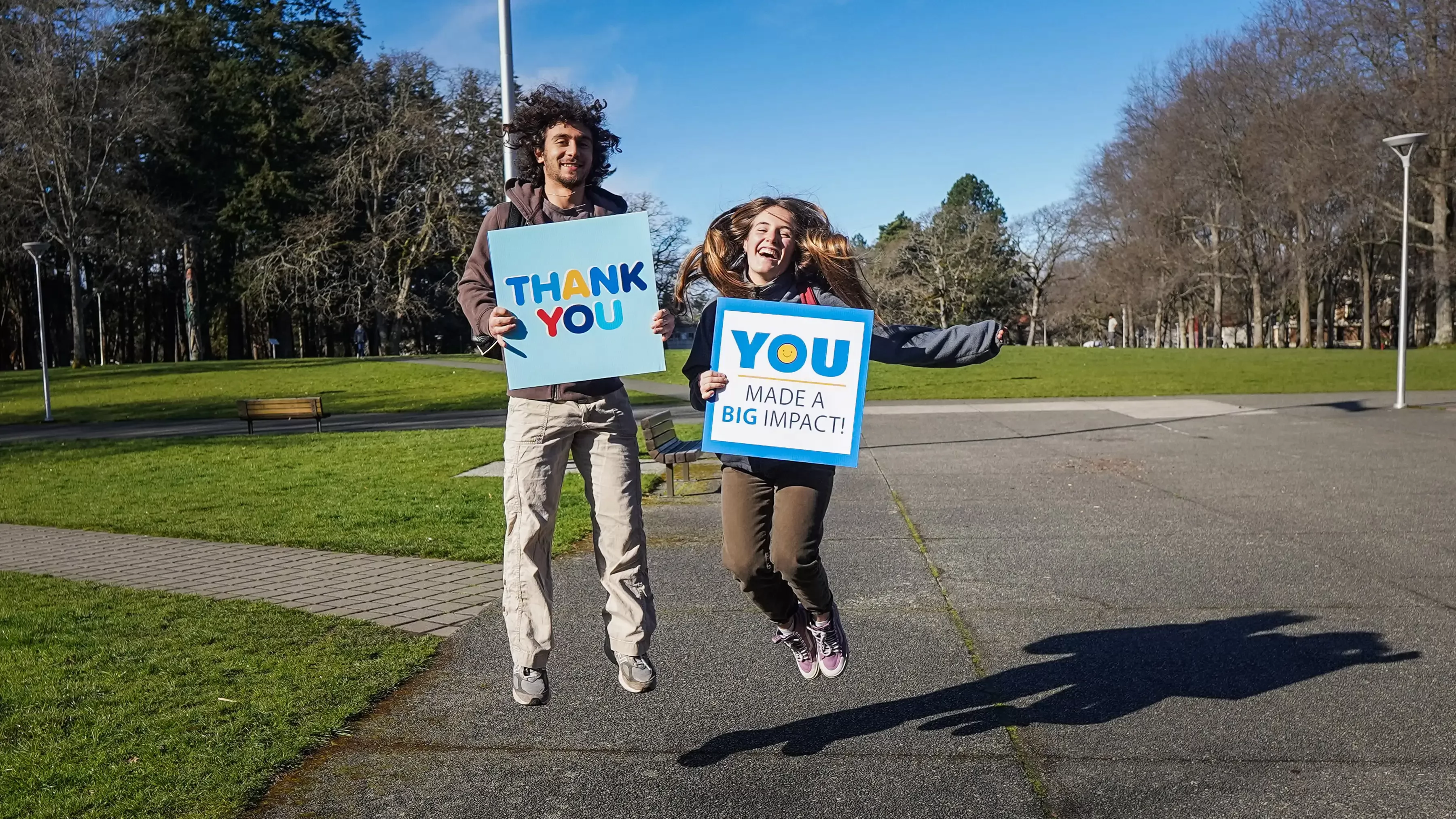 Two people jumping in the air while holding signs that say "Thank you" and "You made a big impact"