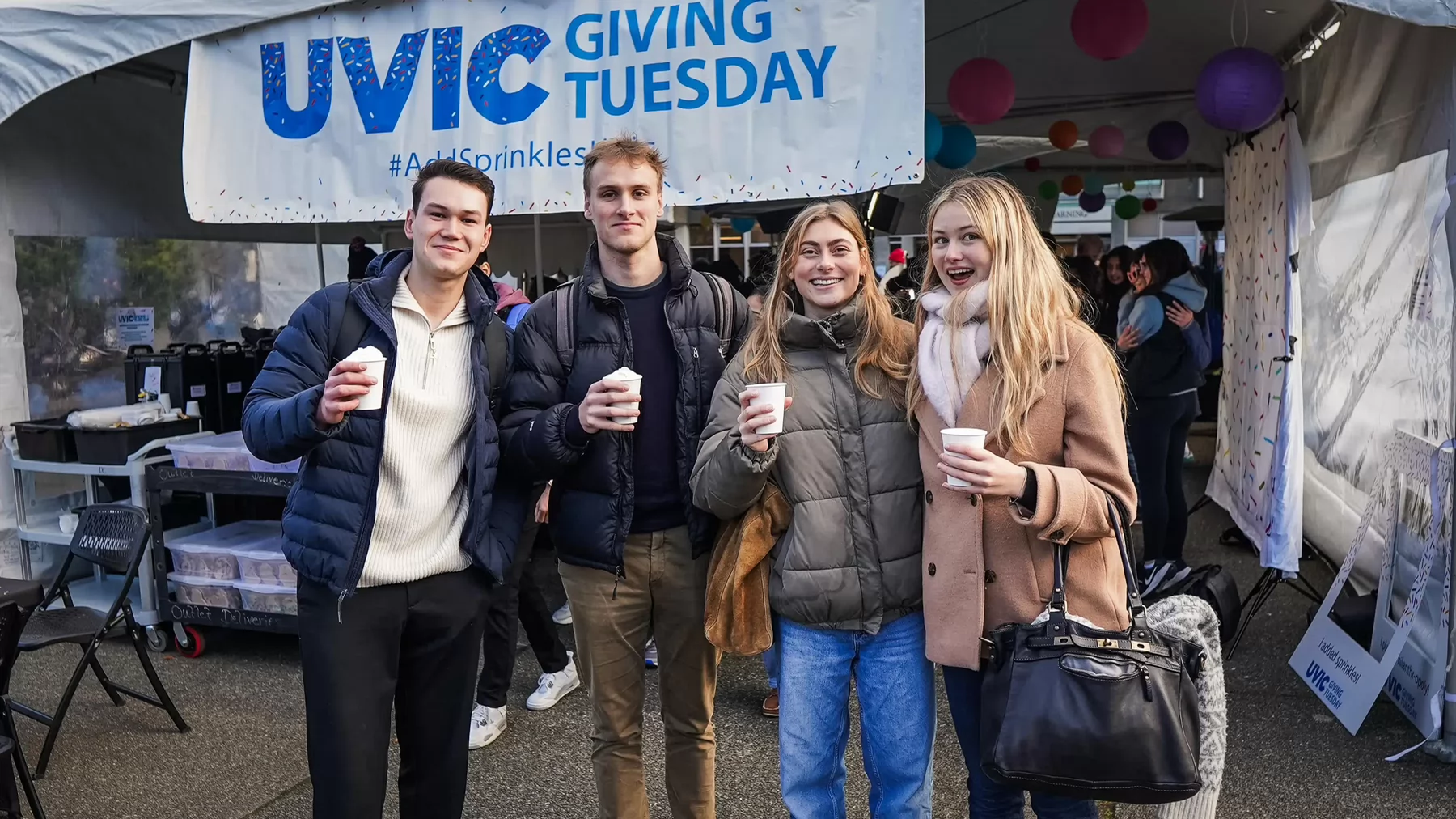 Four students holding cups outdoors at the Giving Tuesday event.