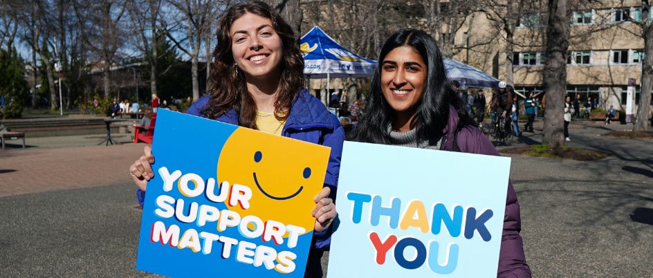 Two students hold signs saying "your support matters" and "thank you" 