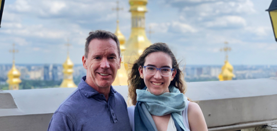 Dale and Sienna stand beside each other smiling at the camera. Behind them are large gold church-like structures